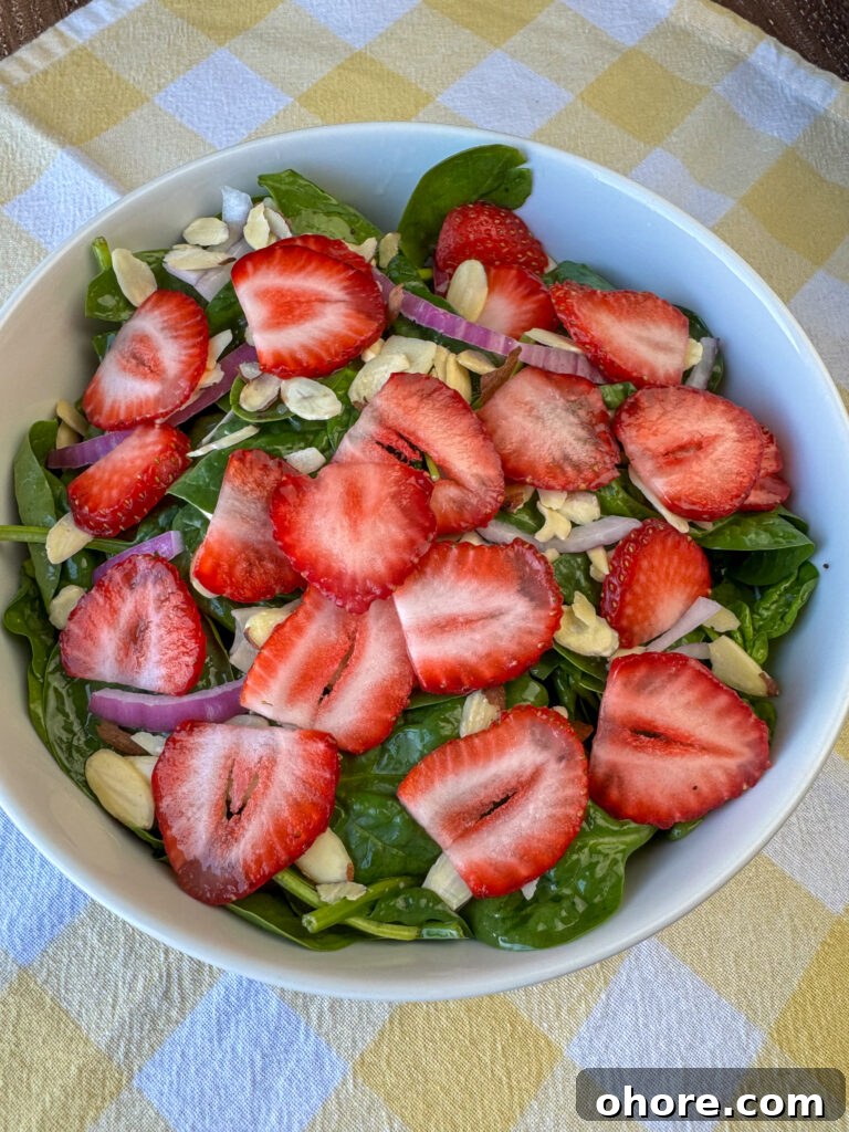 A layer of sliced strawberries coating a bowl of simple spinach salad on a yellow napkin.
