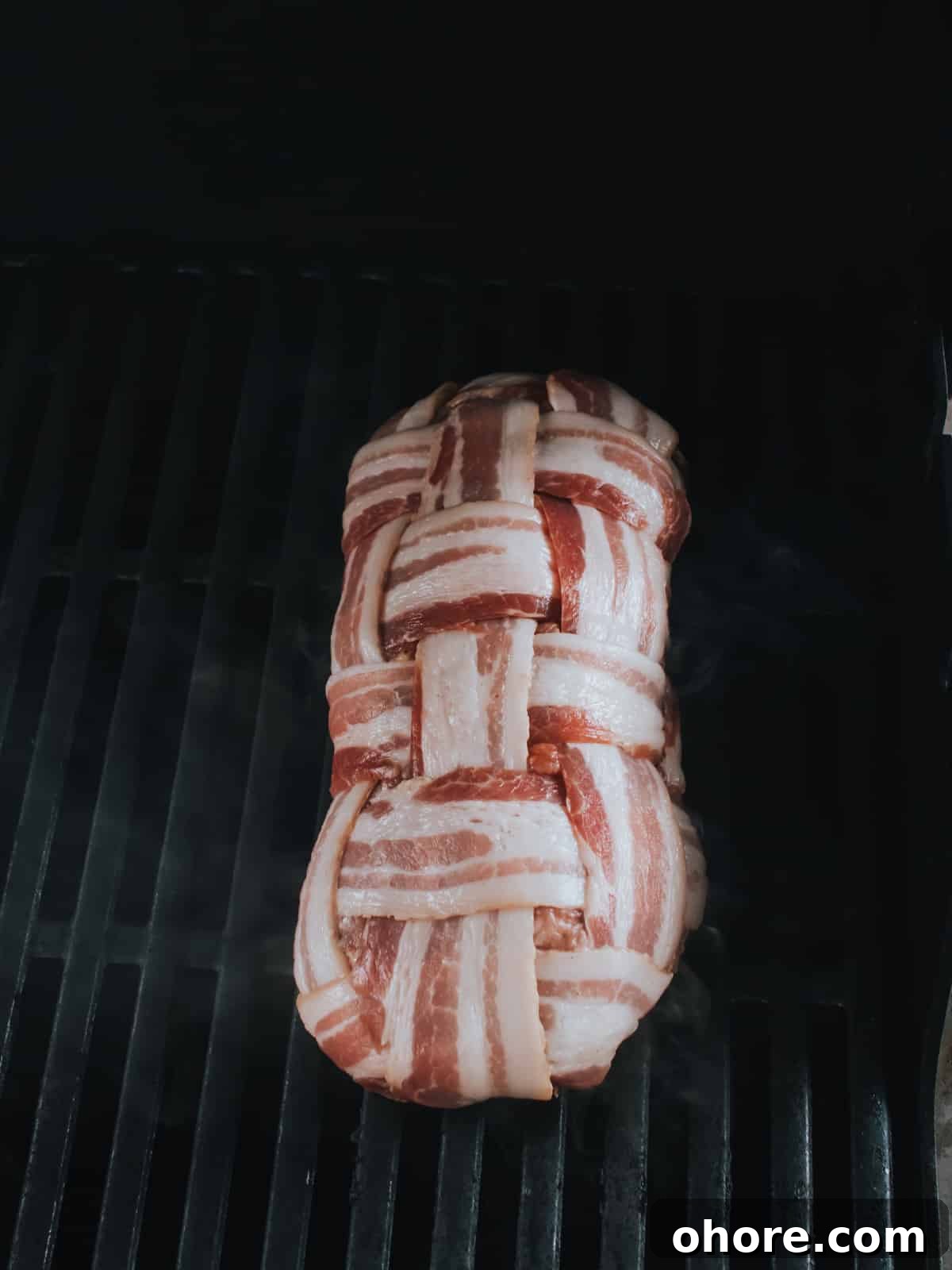 placing loaf of sausage wrapped in bacon on grill