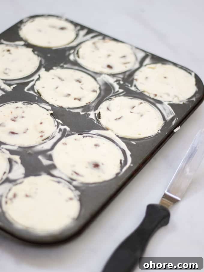 Mini No-Bake Creme Egg Cheesecakes: Bite-Sized Dessert Recipe 4 Mini cheesecakes in a muffin tin with angled palette knife on marble background.