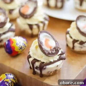 Mini No-Bake Creme Egg Cheesecakes: Bite-Sized Dessert Recipe 7 Mini Creme Egg Cheesecakes with cut creme egg on top on a wooden board.