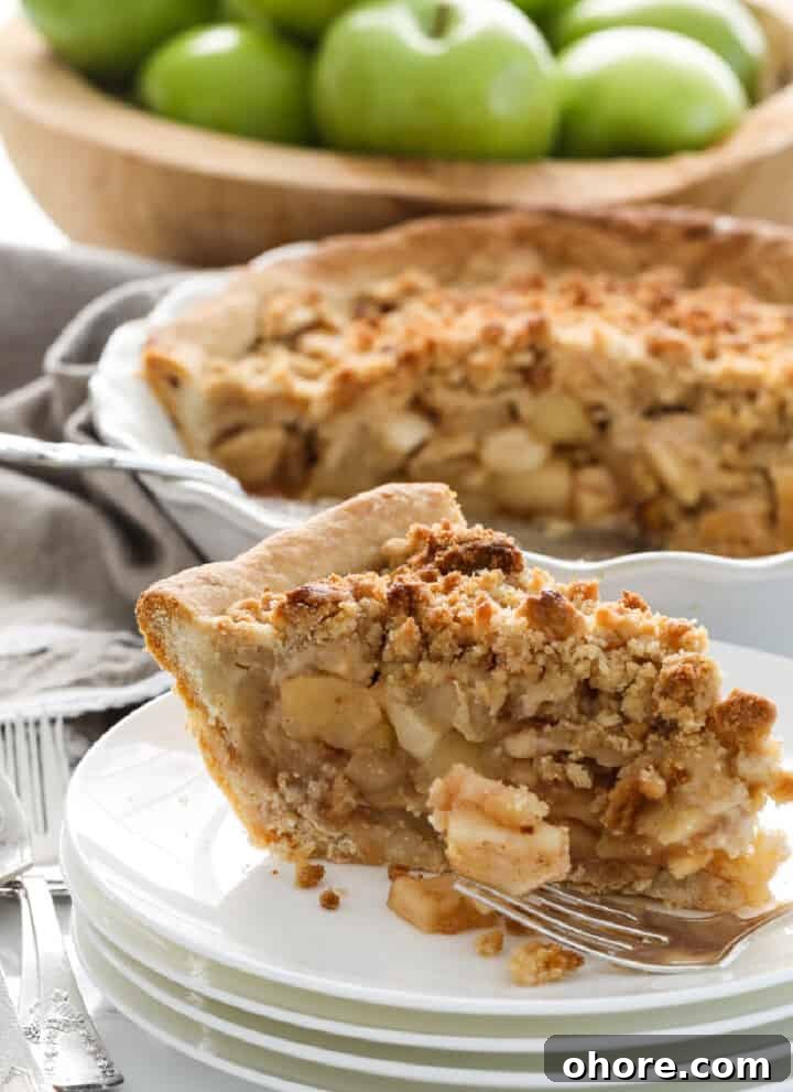 A white pie dish with a slice of apple crumble pie.