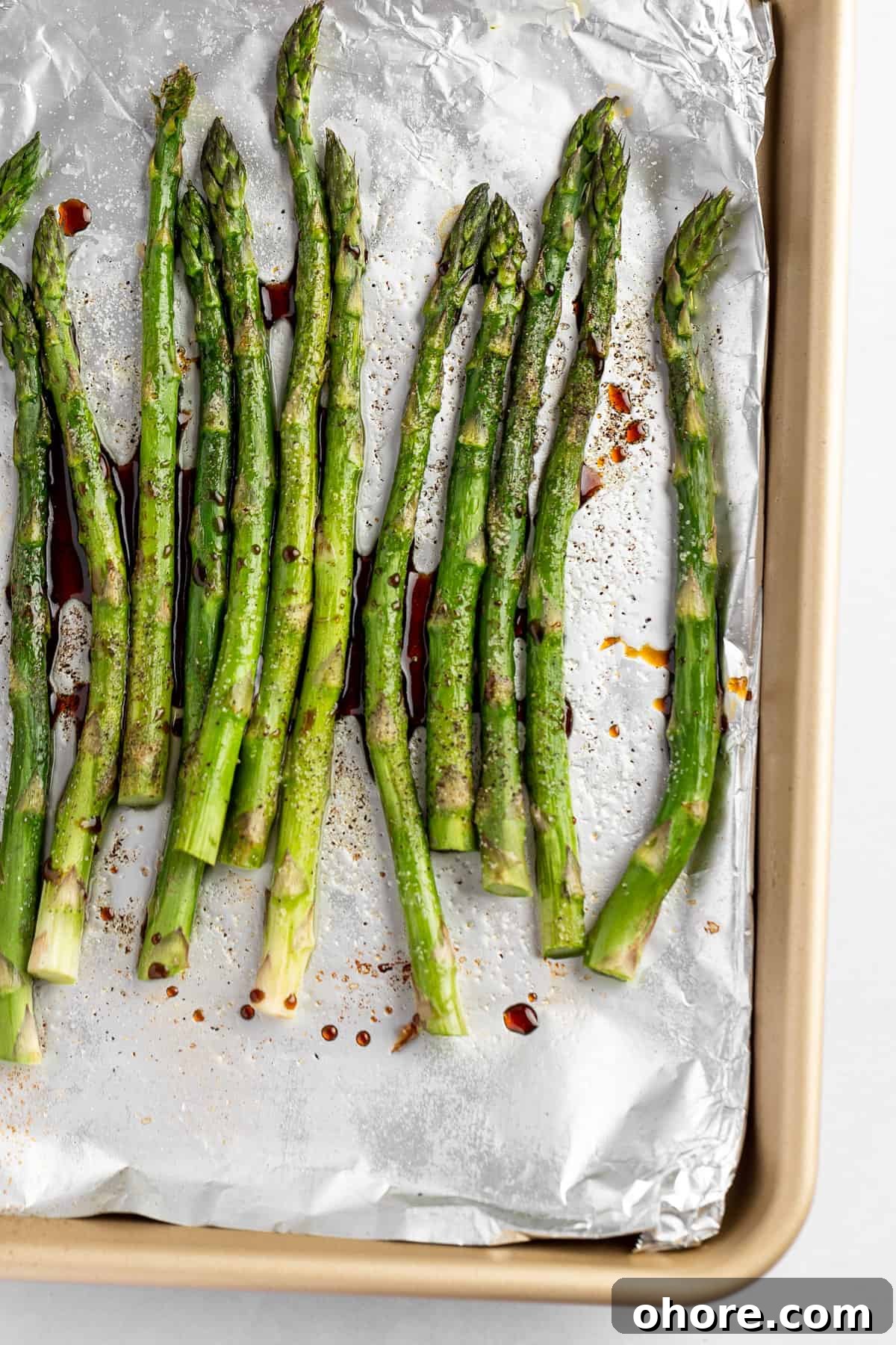 Balsamic-Glazed Asparagus with Garlic and Parmesan 6 Roasted asparagus with balsamic glaze, on a gold baking tray covered in aluminum foil.