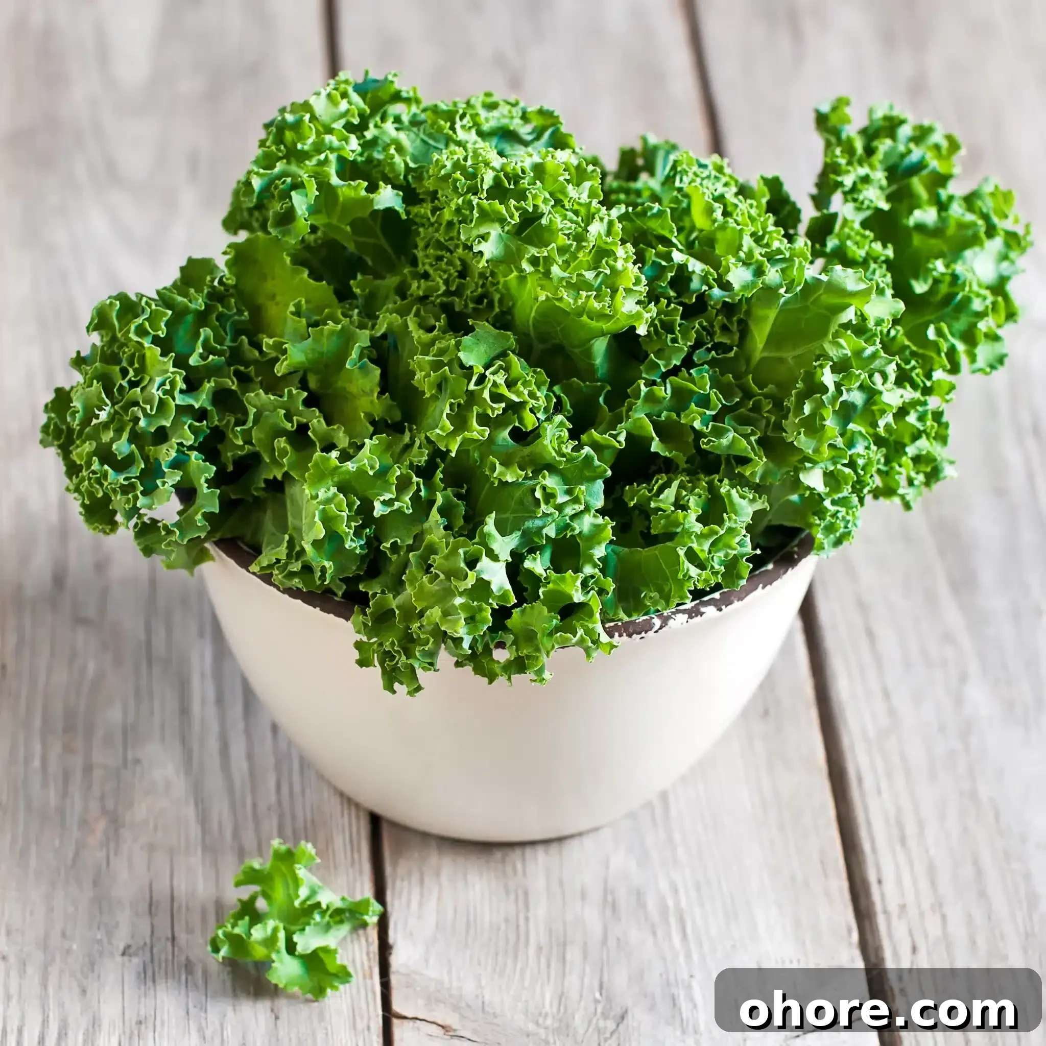 A wooden surface displaying a heaped bowl of kale.