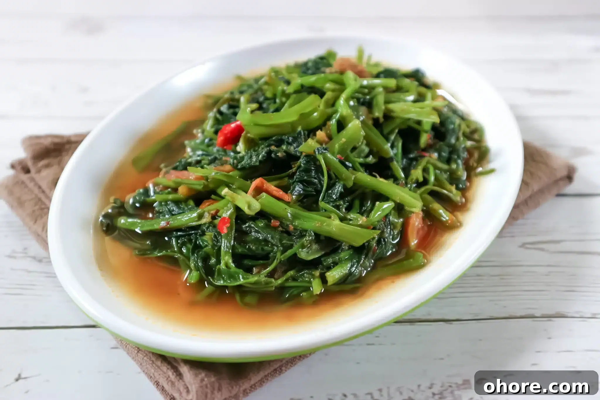 A plate served with steamed kangkung sitting on a brown napkin.