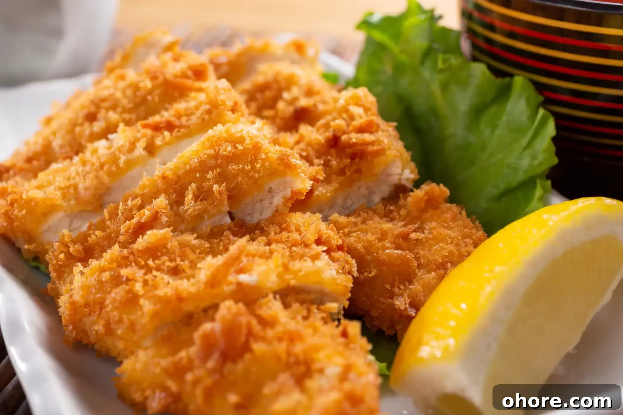 Macro shot of a serving of katsu accompanied by lettuce and lemon.