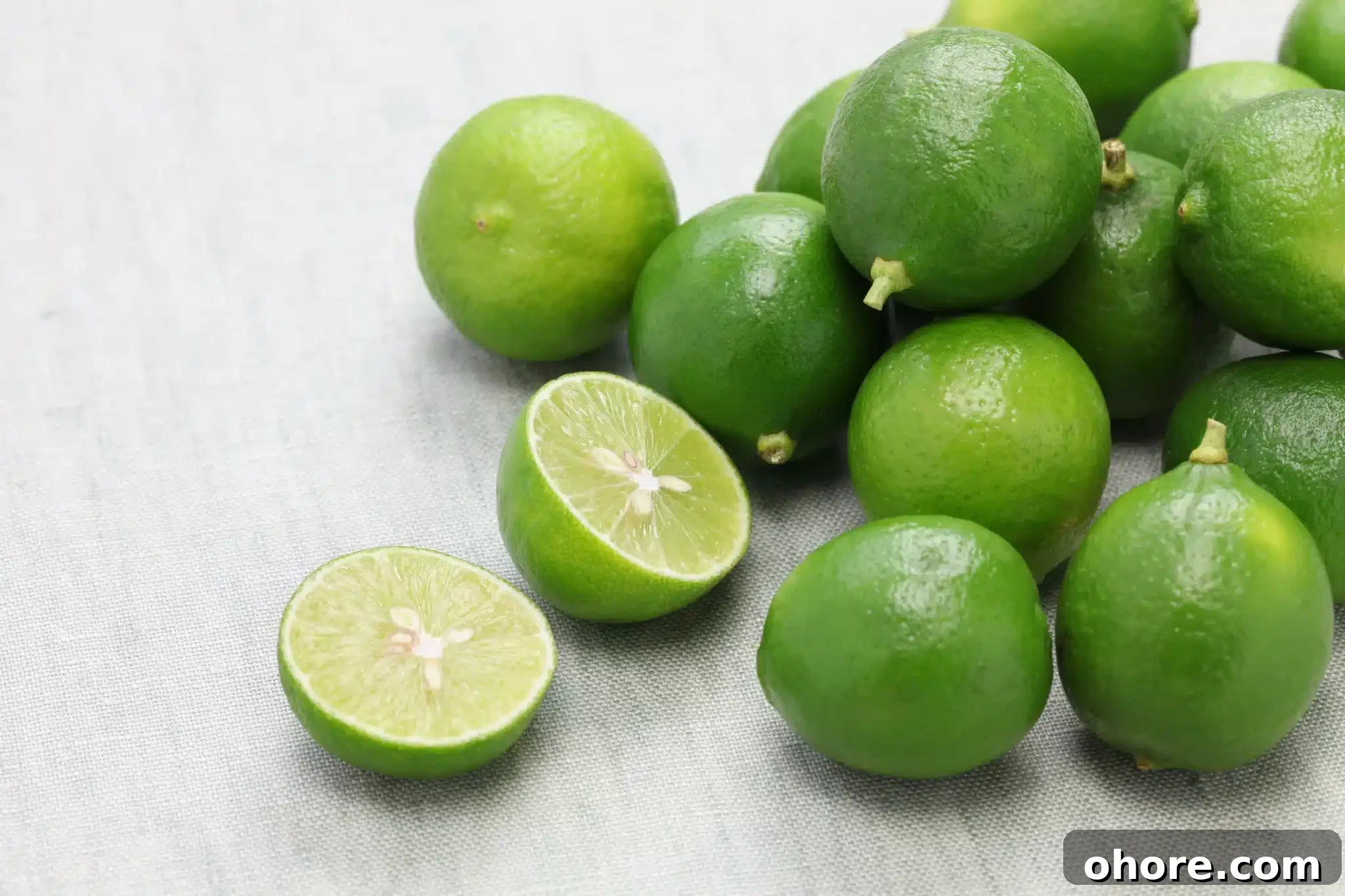 Some entire key limes and a halved one scattered over a tablecloth.