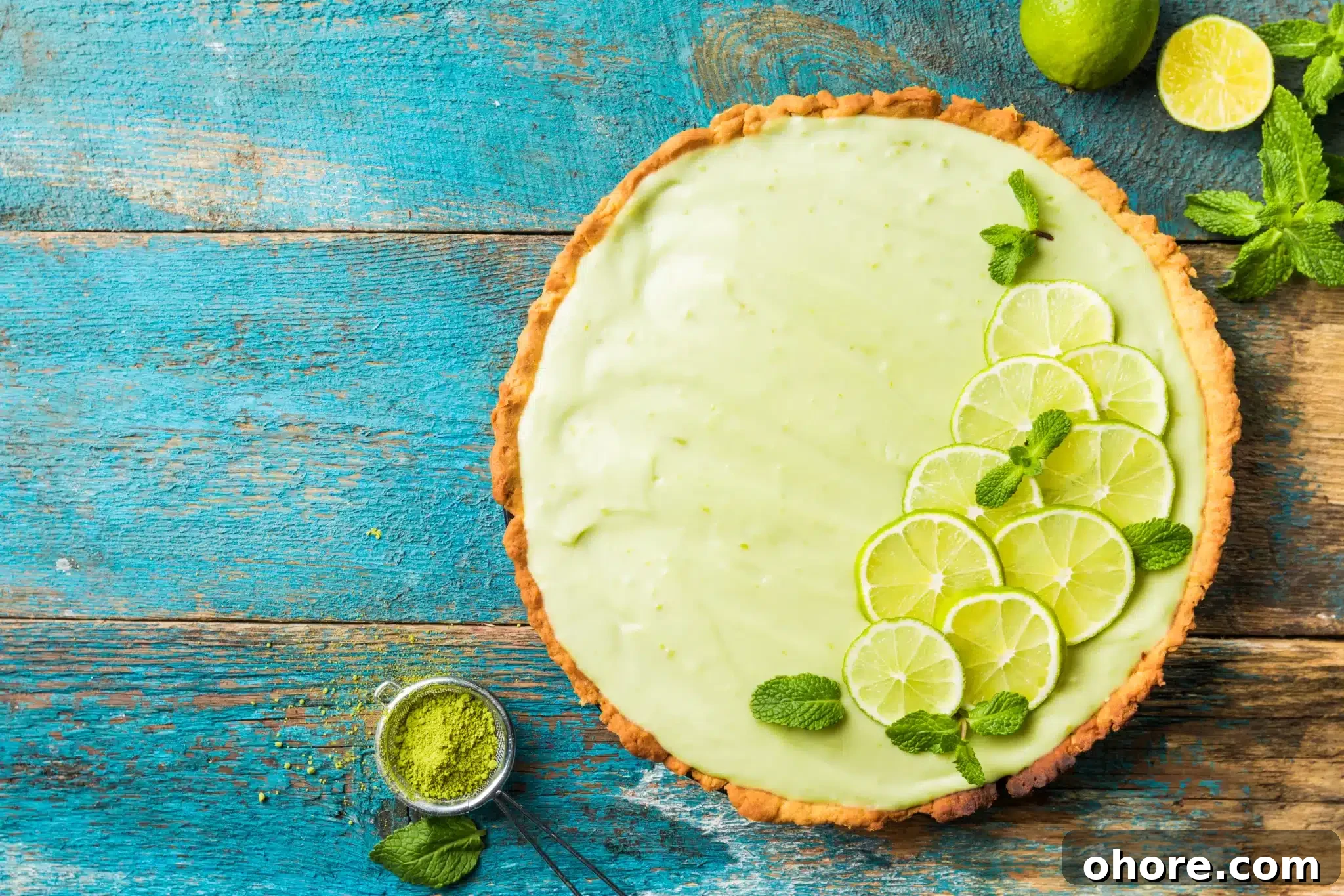 Overhead view of a weathered wooden blue table showing a key lime pie accompanied by some of its ingredients.