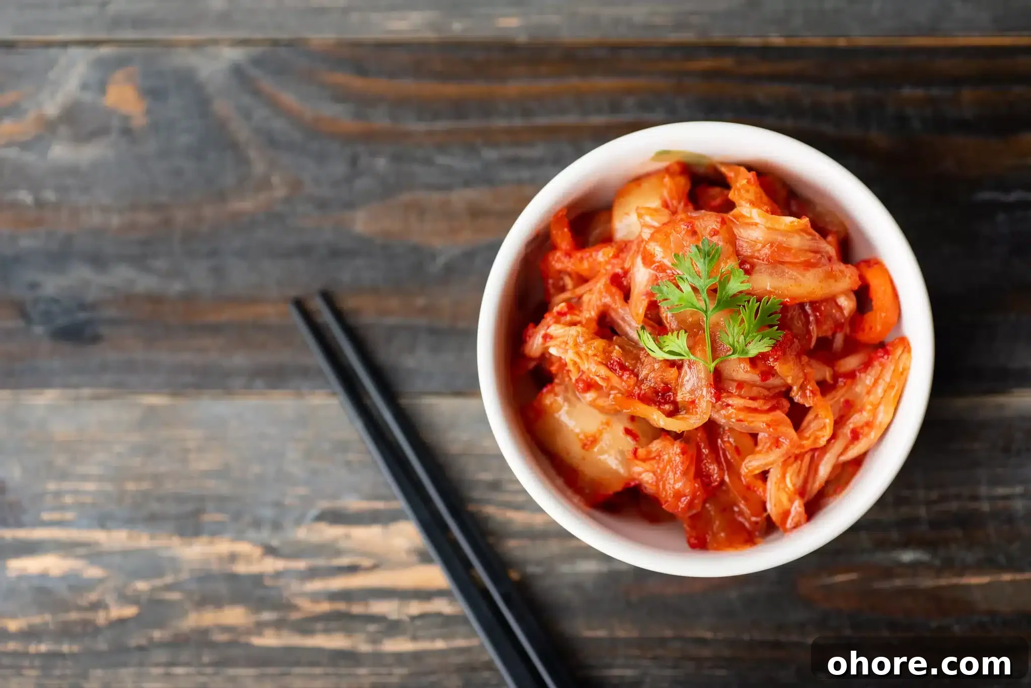 A bowl of kimchi cabbage placed on a wooden background with chopsticks for eating, captured from a top-down perspective.