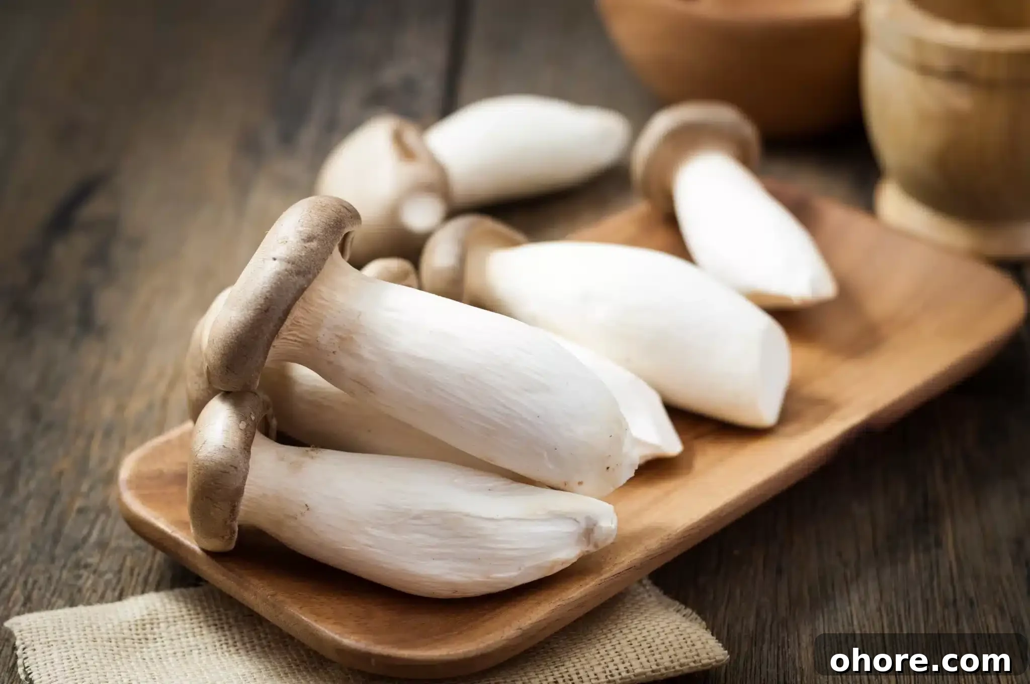 A wooden background featuring some king oyster mushrooms served on a wooden platter.