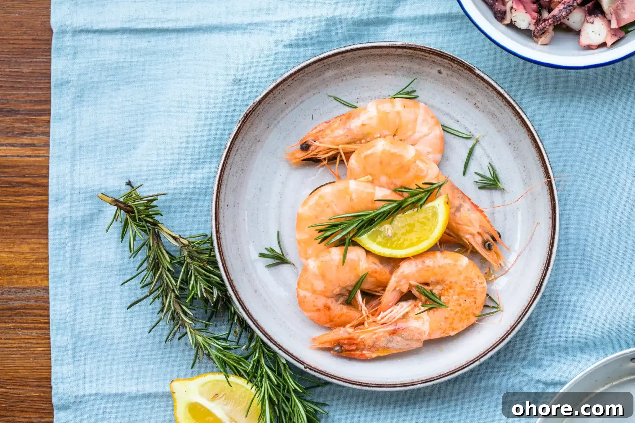 Aerial view of a portion of  king prawns garnished with rosemary and lemon.