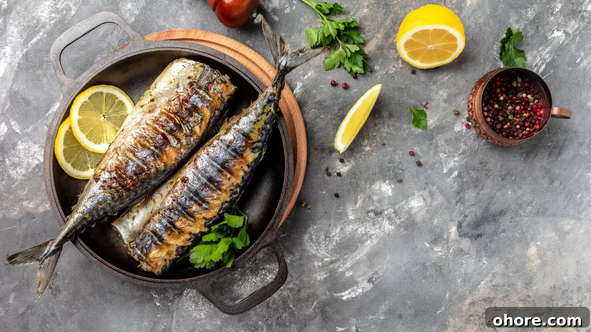 Top view of a concrete table showcasing a pan with grilled kingfish, accompanied by some of the ingredients used to cook it.