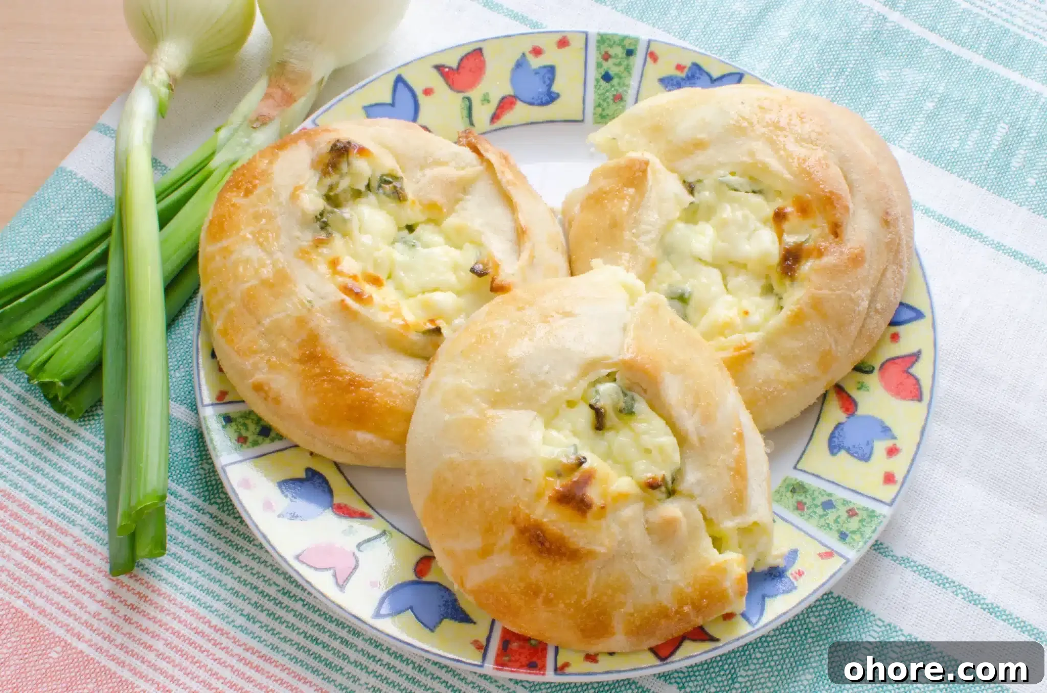 Top view of a plate showing tasty knishes and a couple of green onions nearby.
