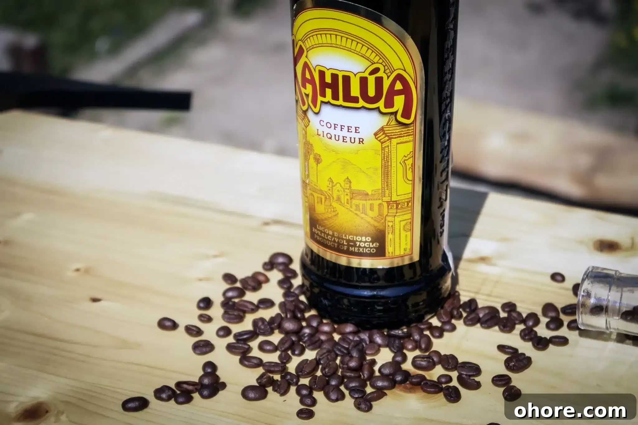 A wooden table showcasing a bottle of Kahlua surrounded by coffee beans.