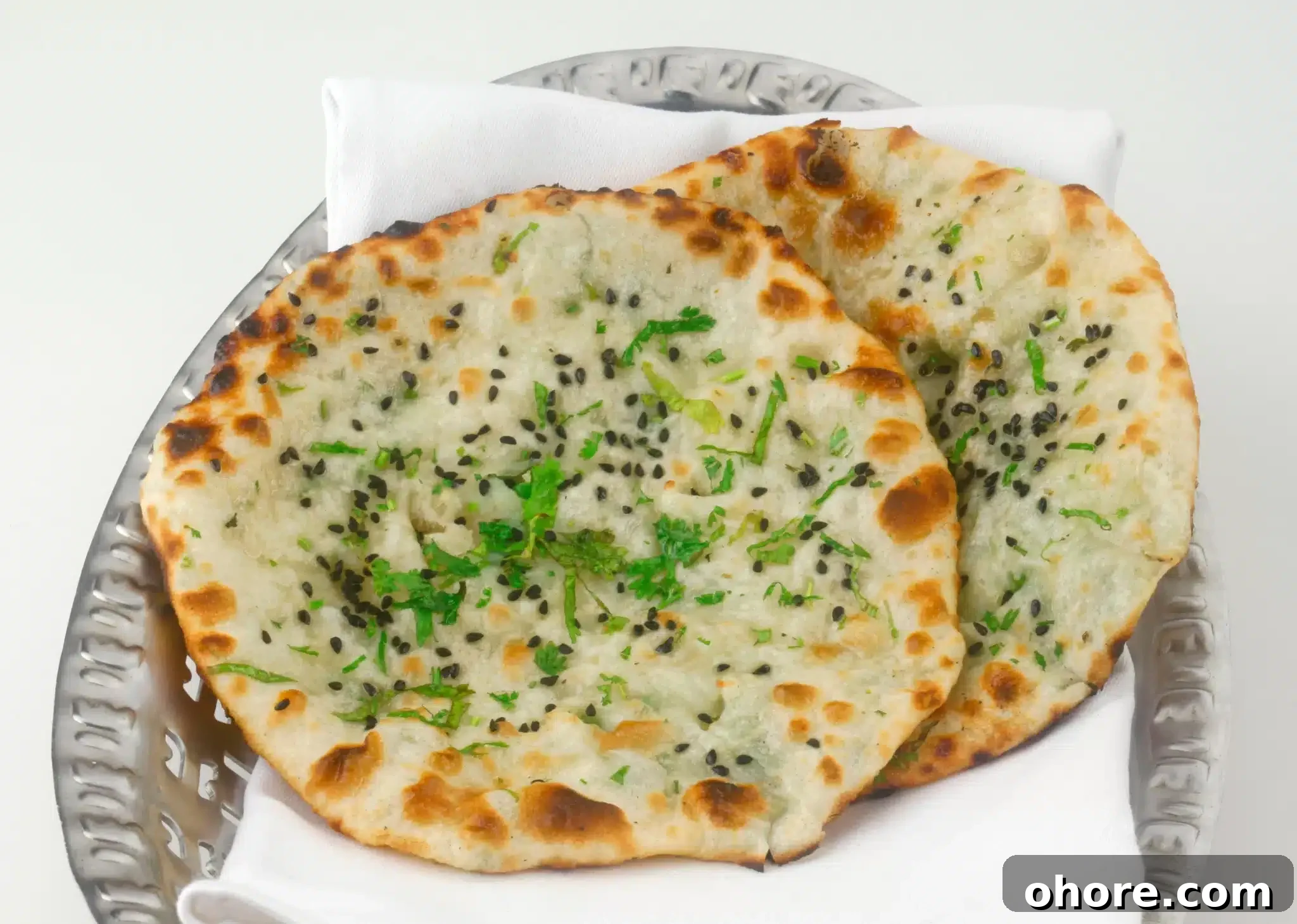 A metal tray holding a pair of Kulcha breads garnished with seeds and herbs.