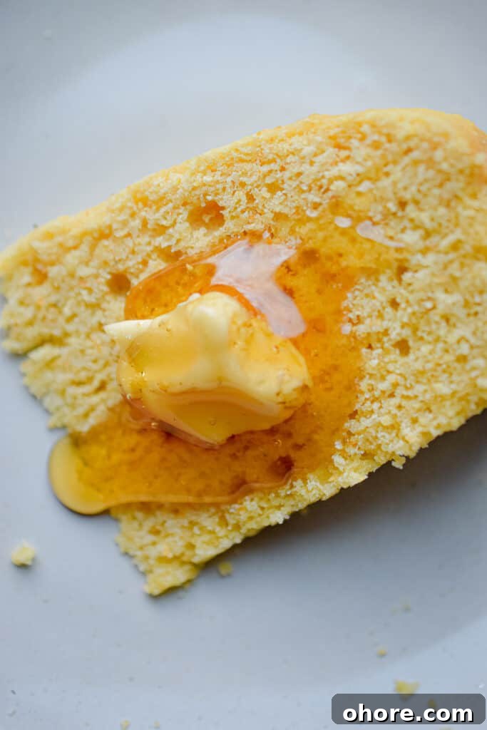 A slice of cornbread is drizzled with honey and has butter on it.