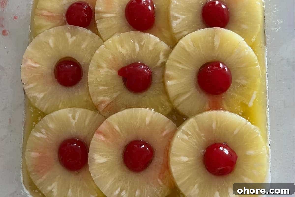 Trisha Yearwood’s Classic Pineapple Upside-Down Cake Recipe 4 Pineapple and cherries lined up in a pan.