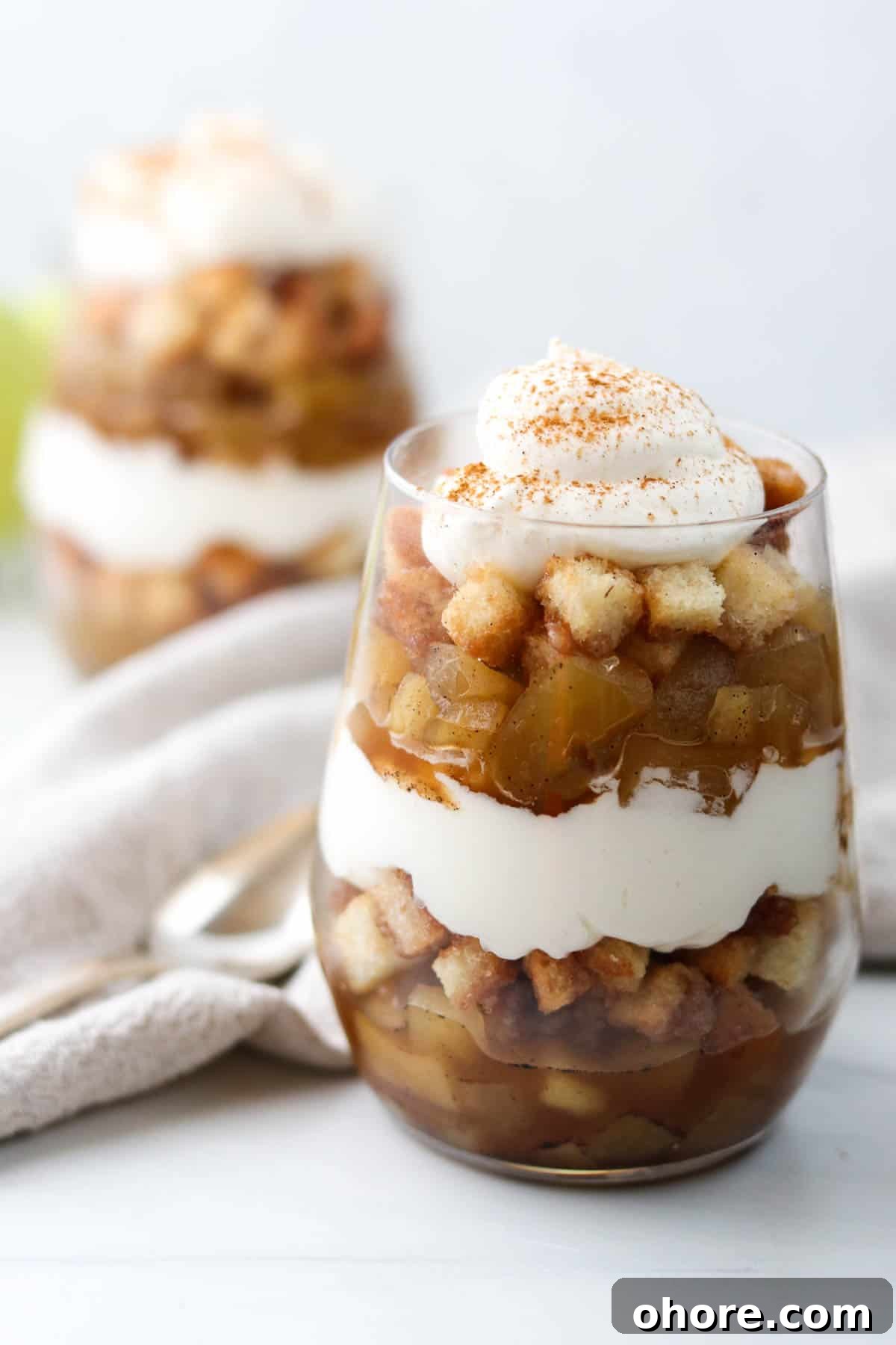 Apple trifle with whipped cream next to a napkin and spoon.