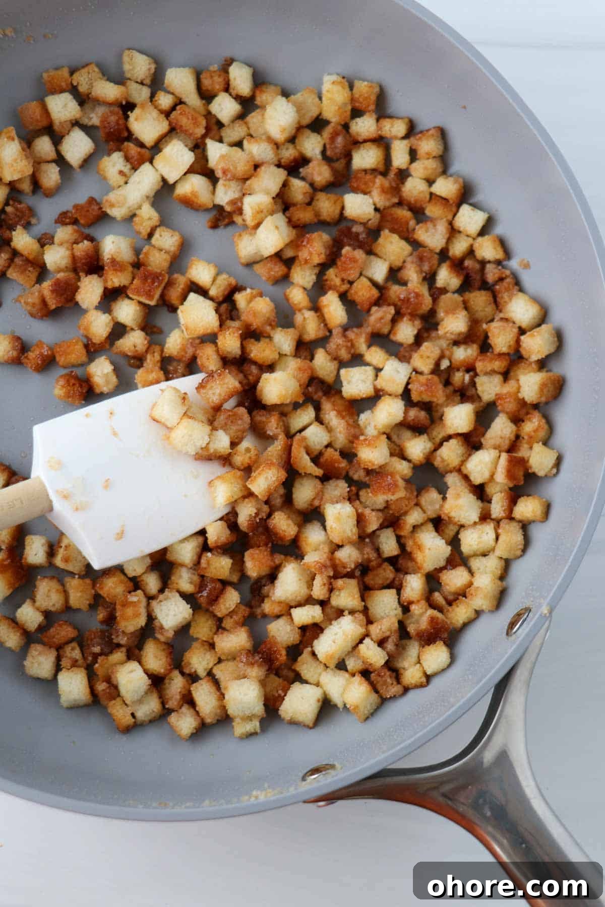 Caramelized bread cubes in a pan with a rubber spatula.