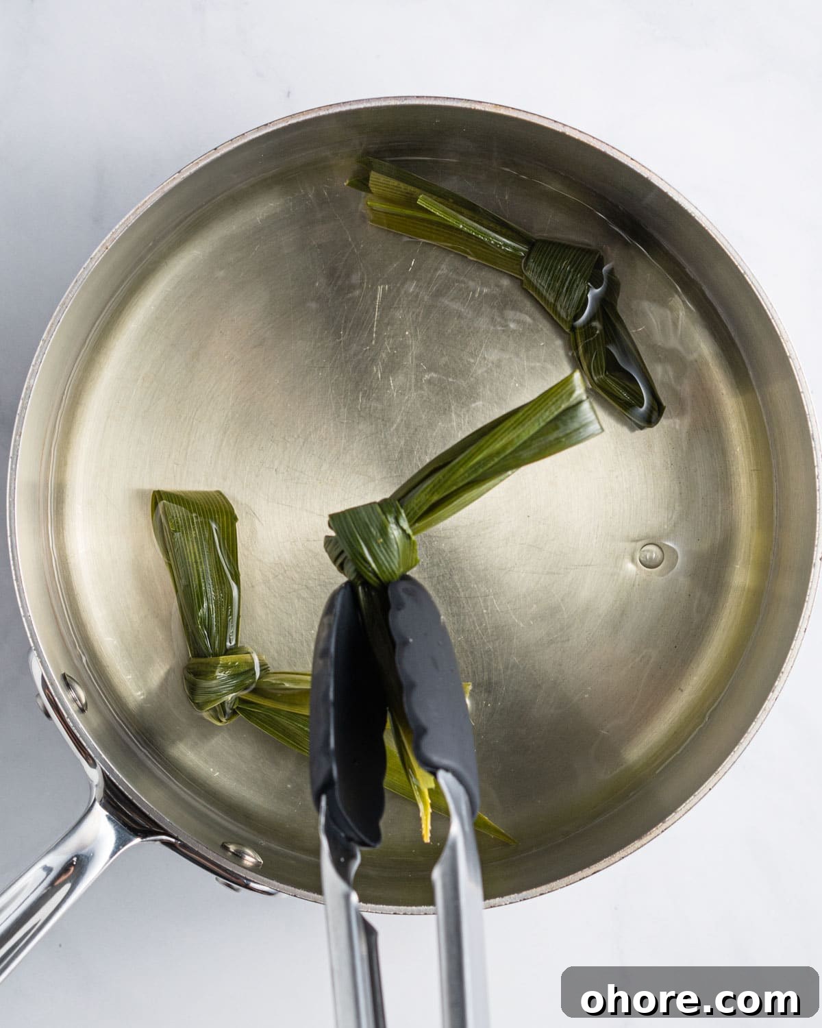 Tongs taking out pandan leaves tied in a knot.