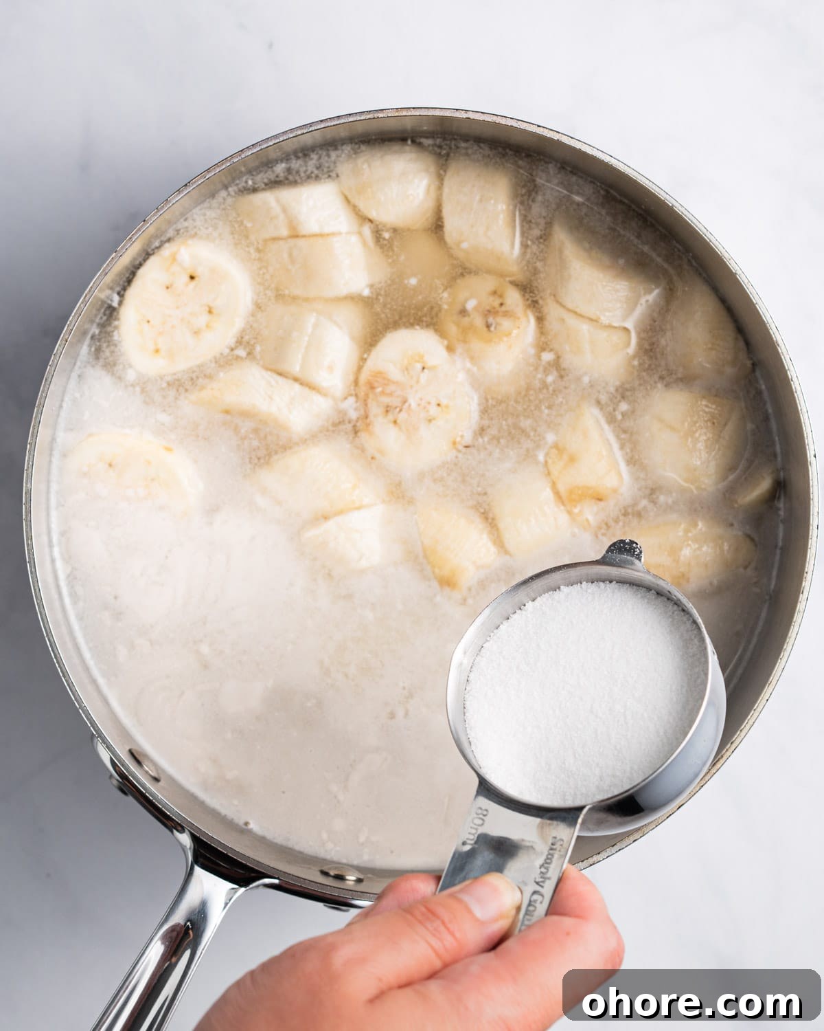 Adding sugar into pot with pandan infused coconut milk, banana, and tapioca pearls.