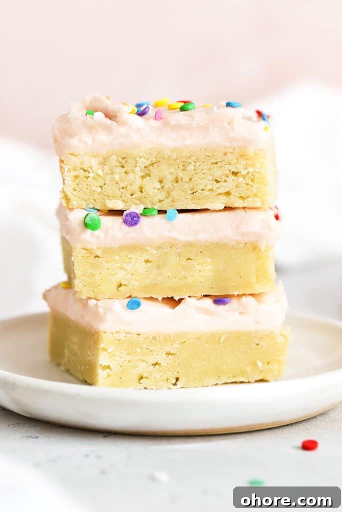 three sugar cookie bars with pink frosting stacked on a white plate
