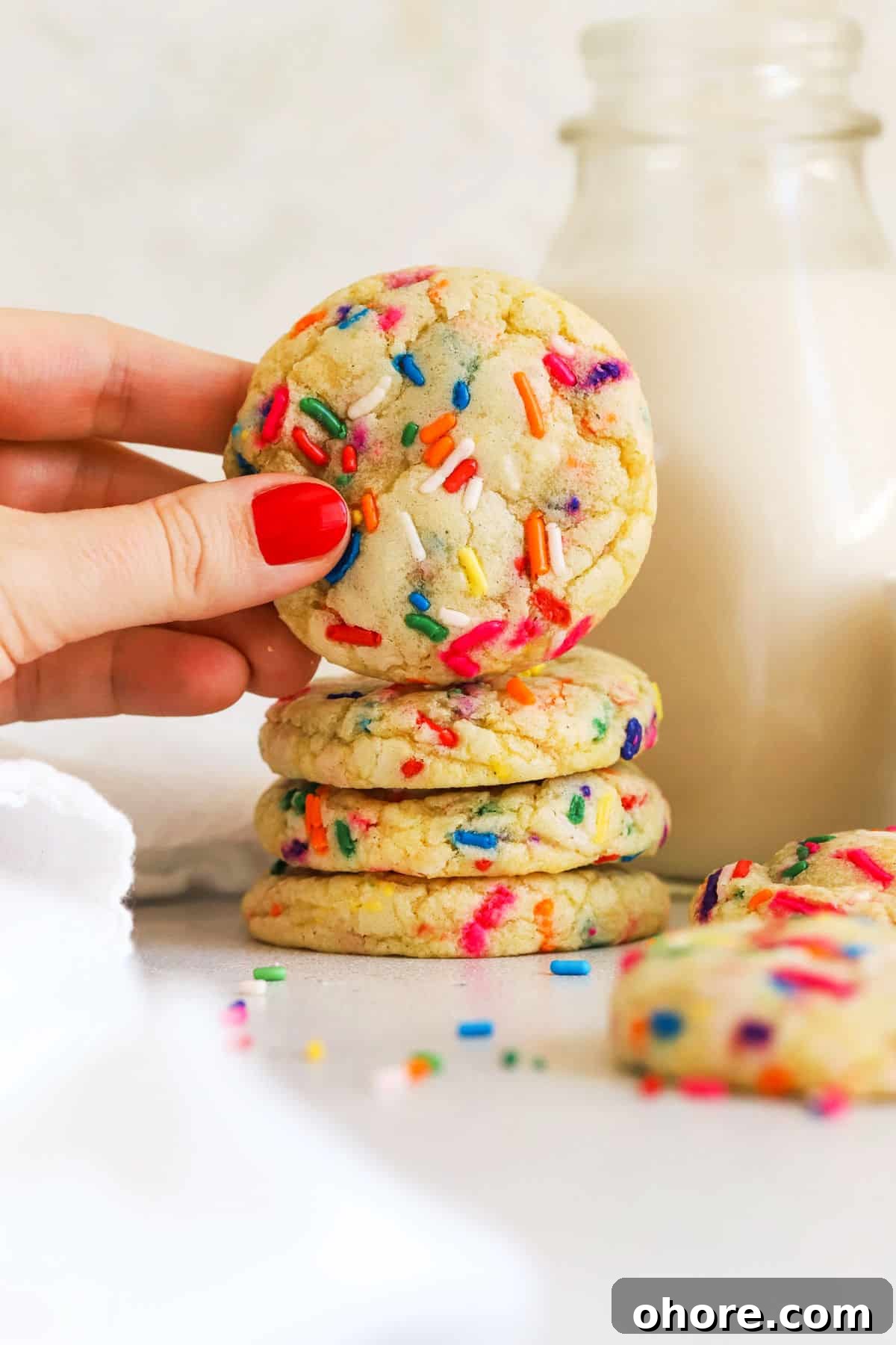 stacking gluten-free sprinkles sugar cookies next to a bottle of milk