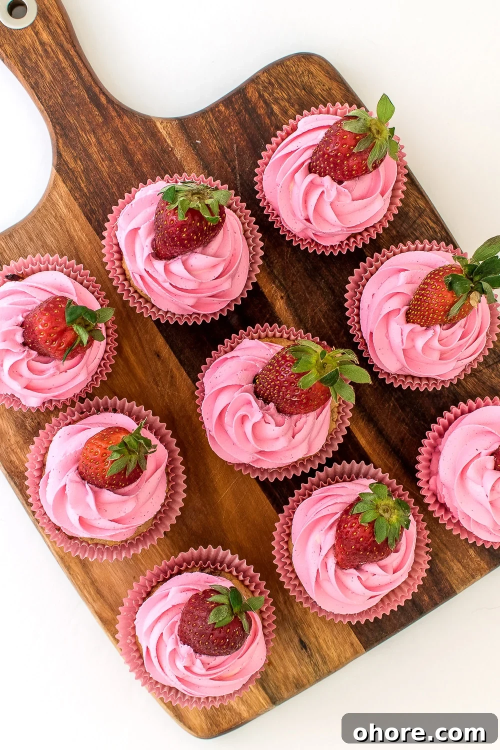 low carb and keto friendly Strawberry cupcake muffins with ruffled pink frosting and a fresh strawberry in pink paper wrappers. 