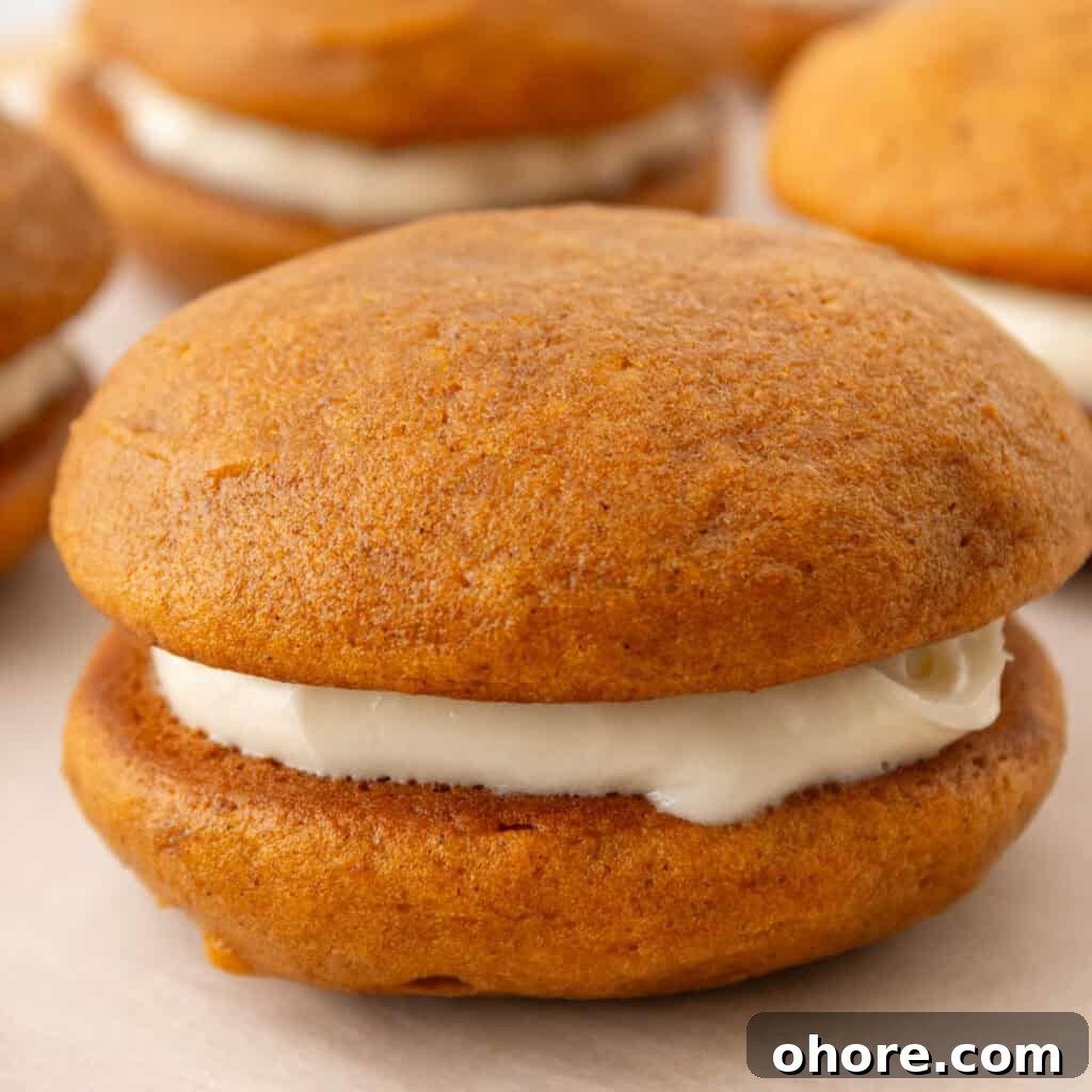 Close-up image of a pumpkin whoopie pie with a creamy filling, resting on a white surface.