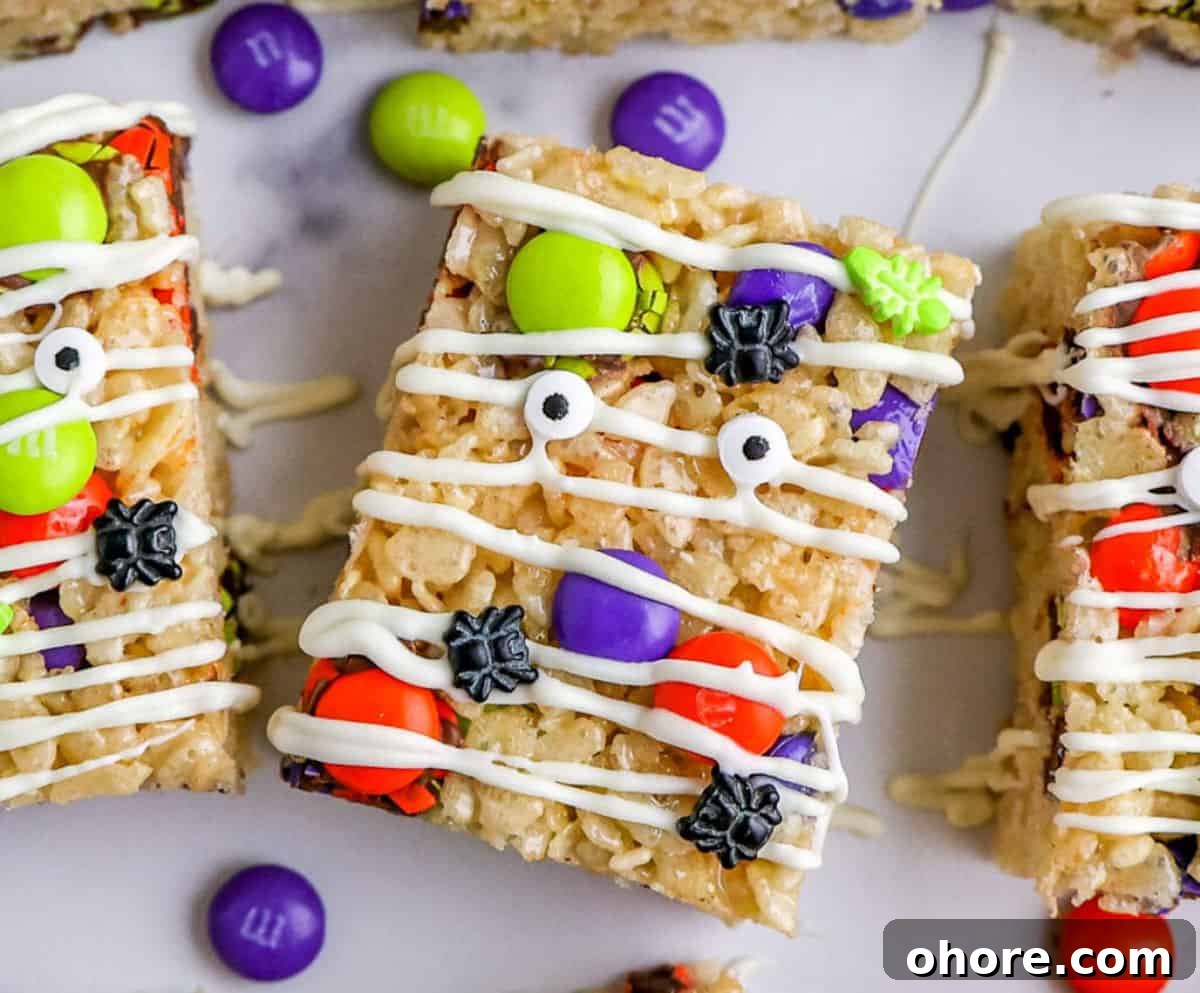 Kid-Friendly Halloween Snack Ideas for Kids 7 Close up of Rice Krispie Treats decorated with Halloween M&Ms, candy eyes and white chocolate drizzle.