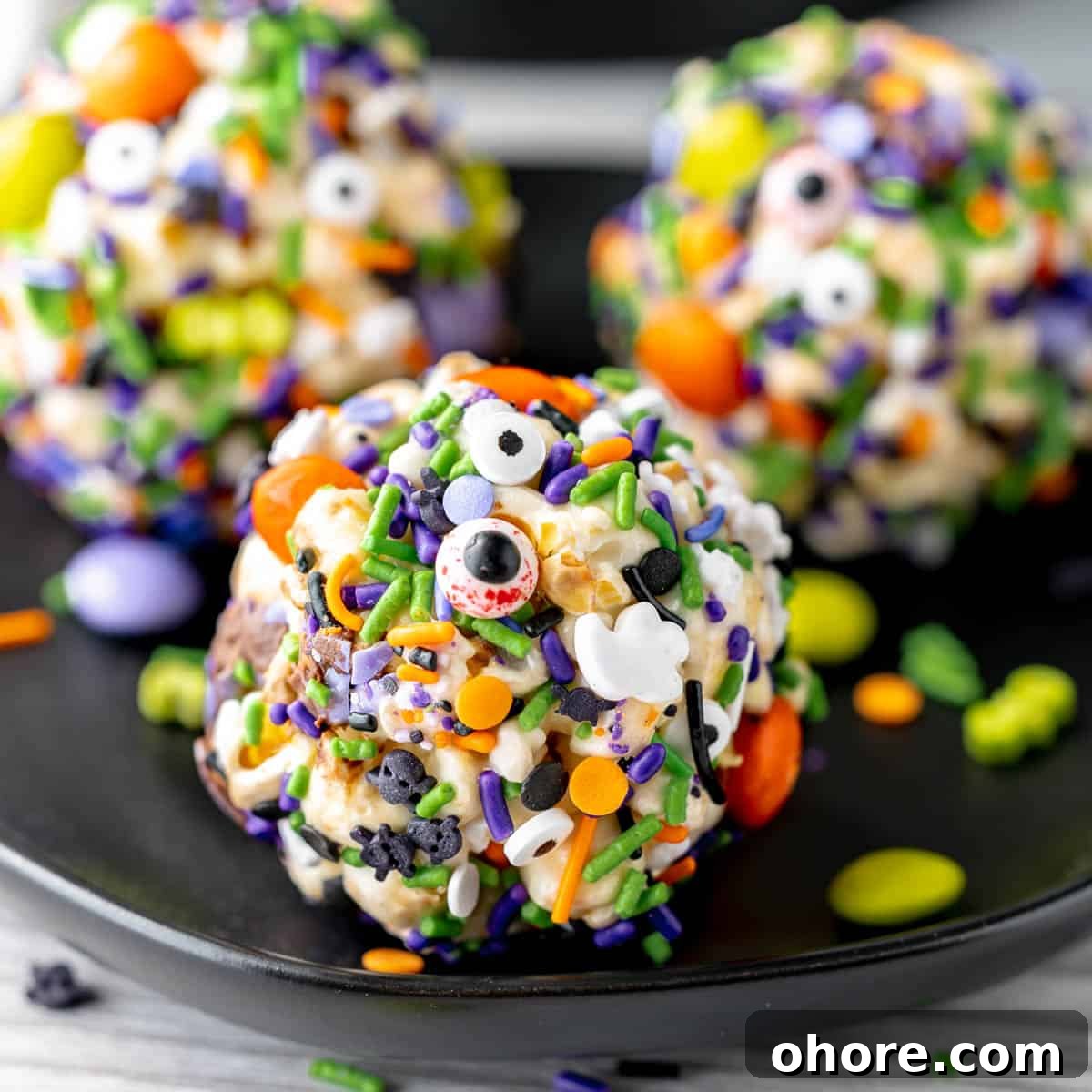 Kid-Friendly Halloween Snack Ideas for Kids 8 Three popcorn balls on a black plate coated in Ghoul's Mix M&Ms and Halloween Sprinkles.