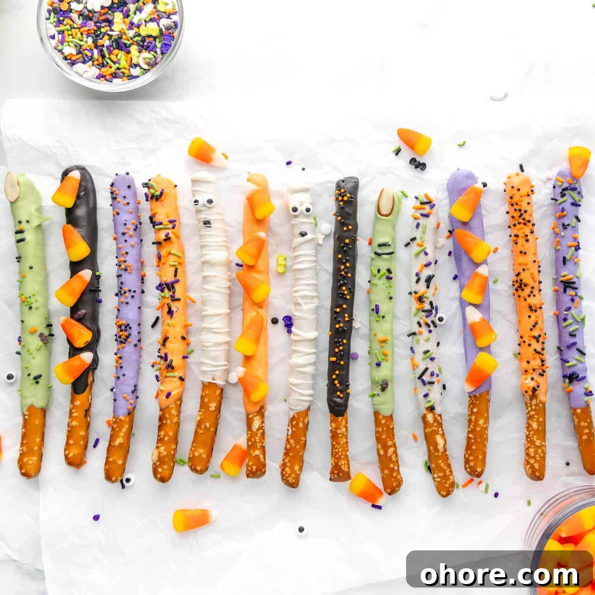 Kid-Friendly Halloween Snack Ideas for Kids 9 A variety of pretzel sticks covered in different colored coatings and decorated with candy eyes, sprinkles, and candy corn, arranged on a white surface.