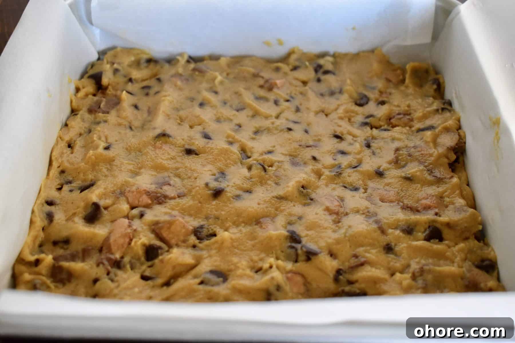 Milky Way Blondies with Caramel and Chocolate Delight 7 blondie batter pressed into the bottom of a parchment lined baking pan.