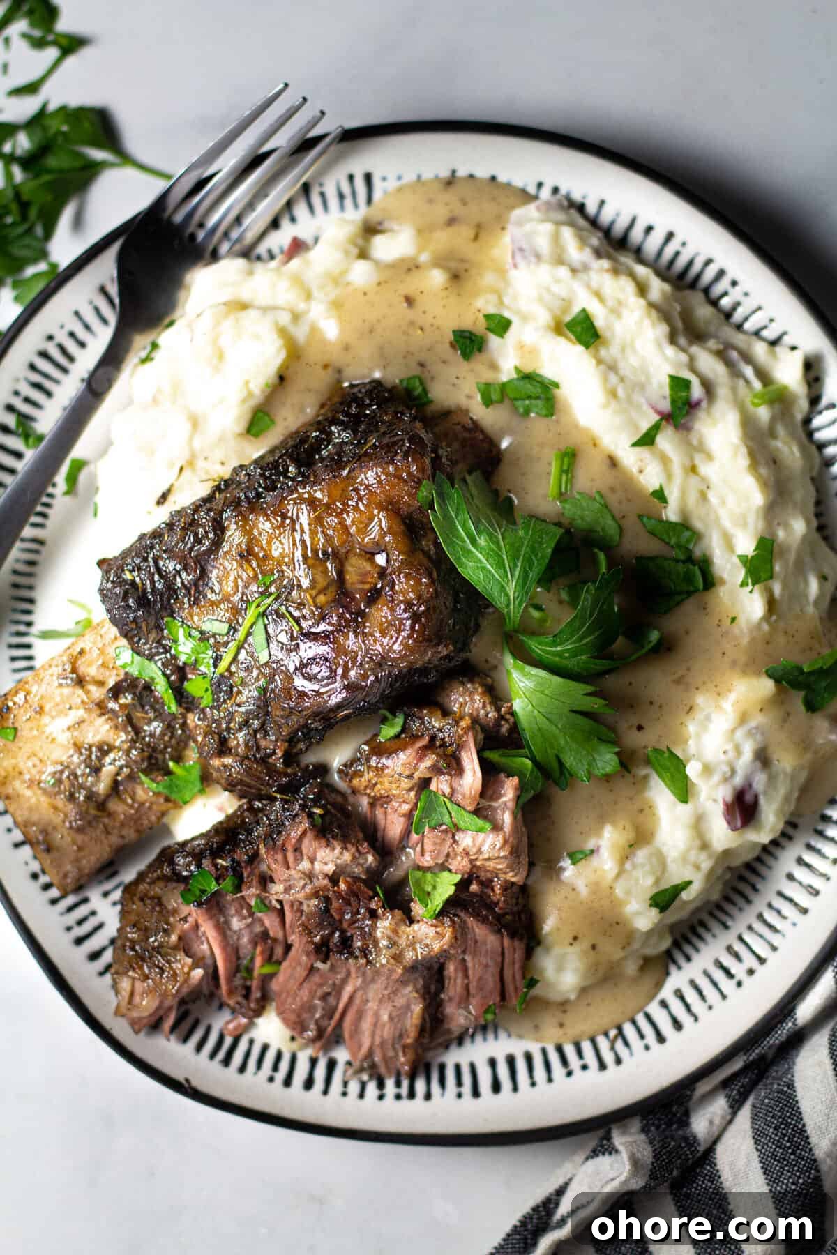Overhead shot of a plate filled with short ribs and homemade mashed potatoes garnished with parsley 
