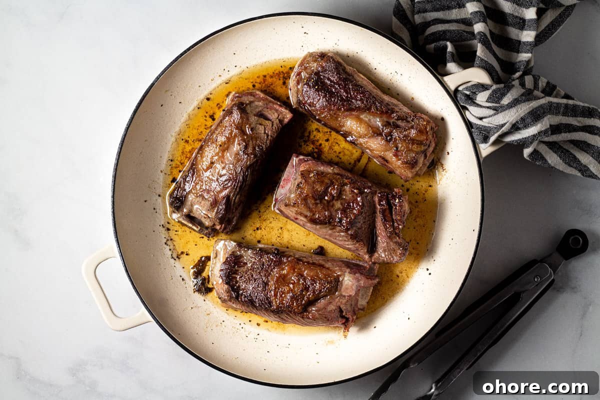 Large pot filled with seared short ribs on a marble counter top 