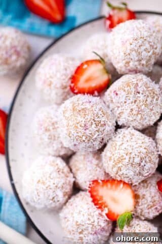 overhead shot of a pile of strawberry coconut truffles covered in shredded coconut and a few sliced strawberries