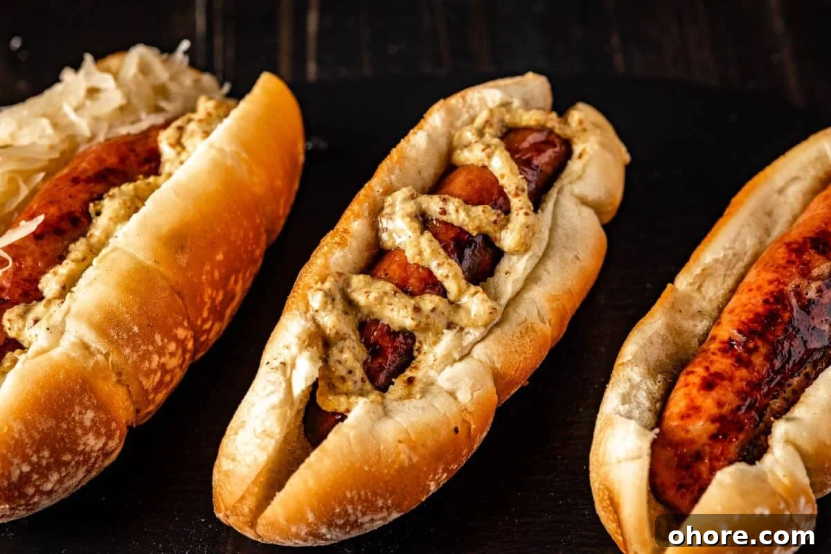 Perfectly Grilled Bratwurst: Juicy Sausage on the Grill 4 A grilled bratwurst on a rolled drizzled with spicy mustard, another topped with sauerkraut, and one plain.