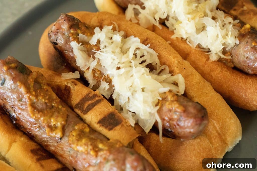 Grilled Bratwurst Recipe Grilled bratwurst in a bun with mustard and sauerkraut, overhead view displayed on a gray plate.
