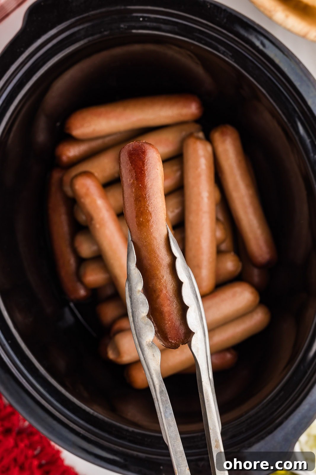 Slow Cooker Hot Dogs: Juicy, Fuss-Free Recipe and Tips 5 black slow cooker with 23 hot dogs cooked with silver prongs holding 1 hot dog
