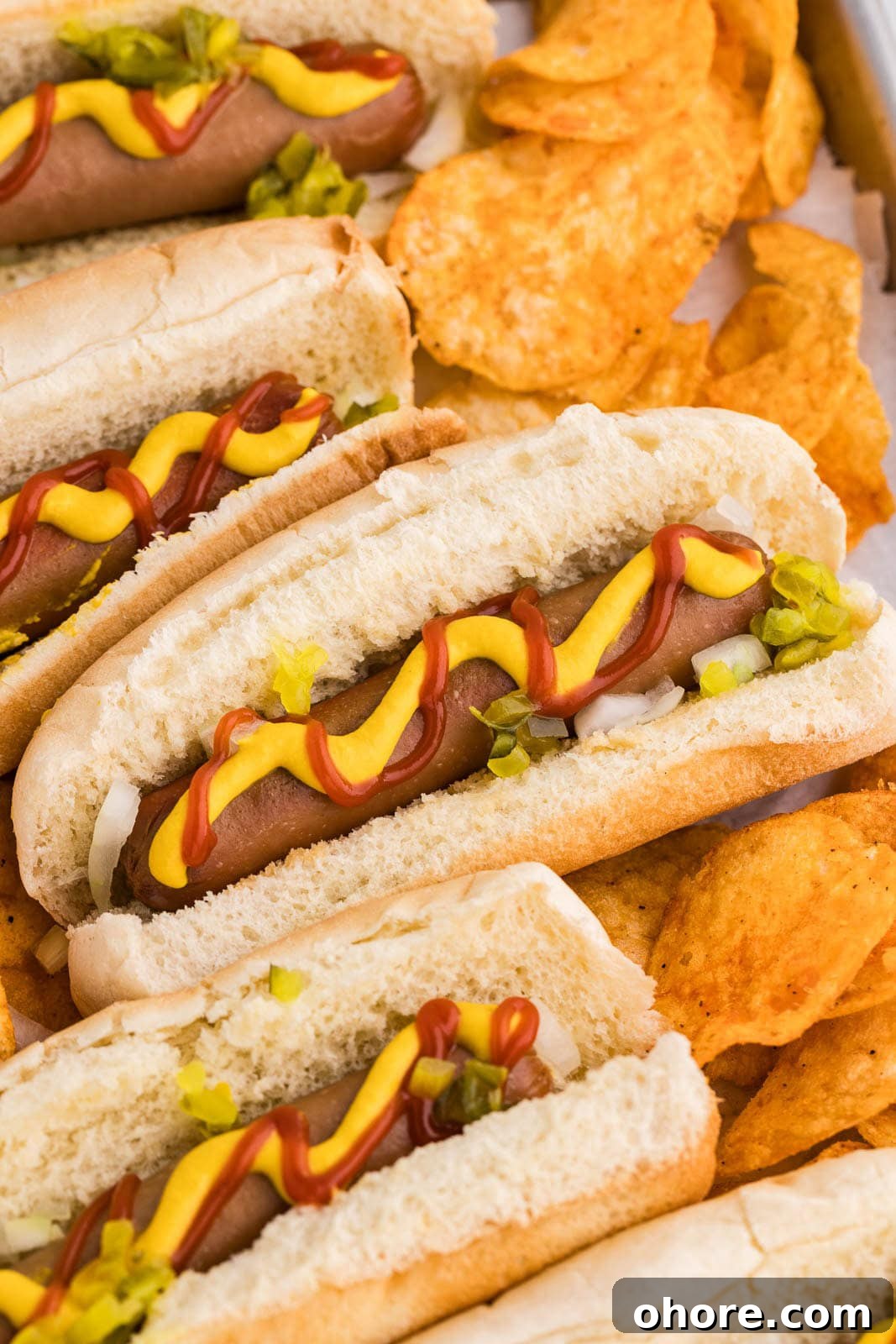 Slow Cooker Hot Dogs: Juicy, Fuss-Free Recipe and Tips 7 closeup of 4 hot dogs in buns garnished with ketchup, mustard, relish, onions interspersed with bbq potato chips