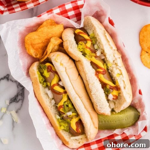 Slow Cooker Hot Dogs: Juicy, Fuss-Free Recipe and Tips 8 overhead view of red and white checked paper tray holding 2 dressed hotdogs, bbq potato chips and dill pickle surrounded by white bowl of onions, red bowl of potato chips and other trays with hot dogs