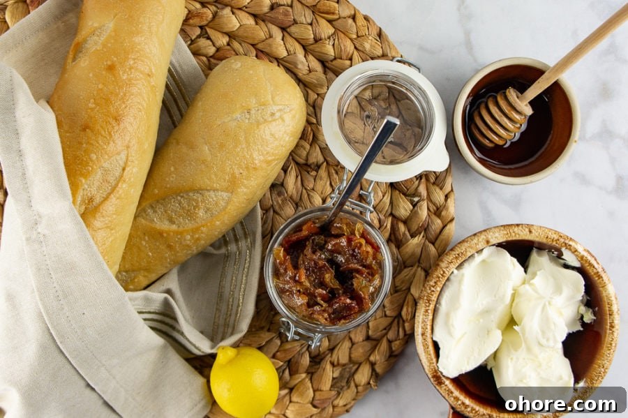 Savory Bacon Jam Crostini Recipe for Entertaining 3 two baguettes with a bowl of creamy cheese, beside a jar of bacon jam, a bowl of honey, and a lemon
