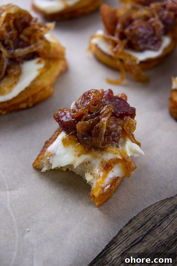 Savory Bacon Jam Crostini Recipe for Entertaining 6 a bacon jam crostini with a bite taken out of it on a parchment paper with other crostinis around it.