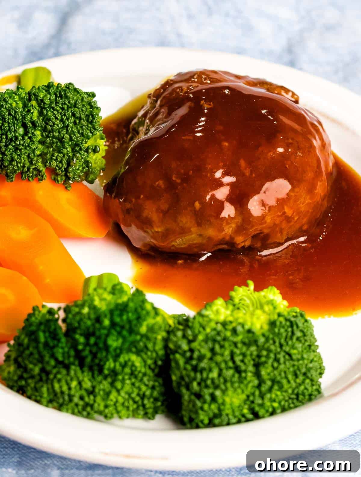 Japanese Hambagu (Hamburger Steak) Recipe — Authentic Pan-Fried Steak 2 Juicy, tender Japanese hamburger steak (hambāgu ハンバーグ) covered in tangy brown gravy on a white plate next to carrots and broccoli.