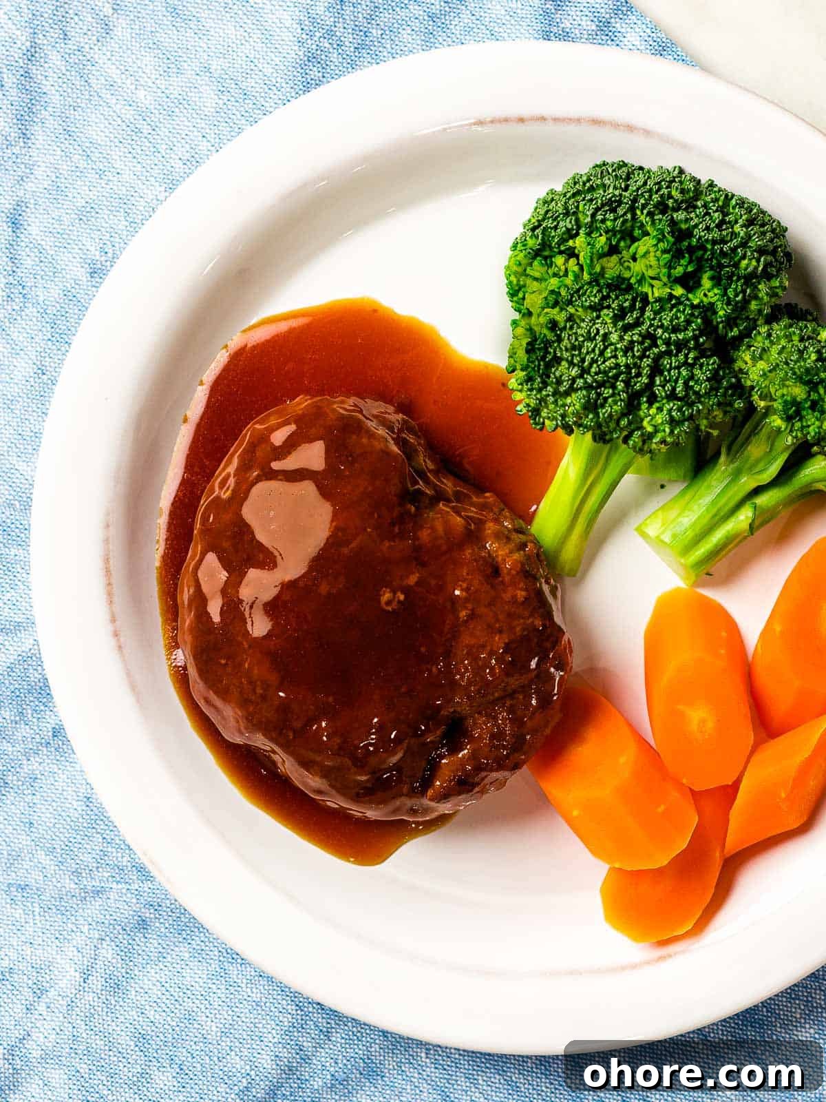 Japanese Hambagu (Hamburger Steak) Recipe — Authentic Pan-Fried Steak 13 Japanese hamburger steak (hambāgu ハンバーグ) covered in tangy brown gravy on a white plate next to carrots and broccoli.