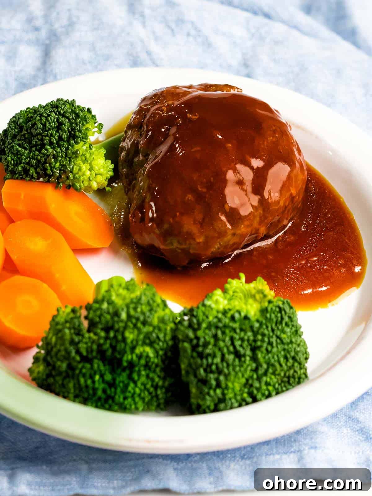 Japanese Hambagu (Hamburger Steak) Recipe — Authentic Pan-Fried Steak 14 Juicy, tender Japanese hamburger steak (hambāgu ハンバーグ) covered in tangy gravy on a white plate next to carrots and broccoli.