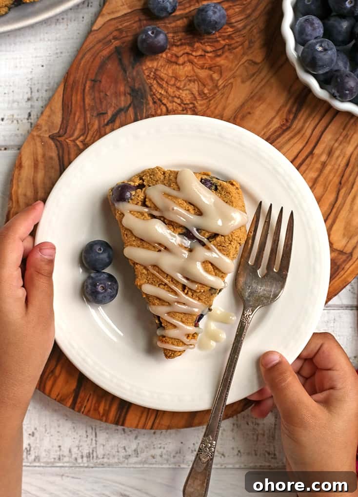 Paleo Blueberry Scones Recipe – Flaky, Grain-Free Breakfast Treat 6 a paleo blueberry scone on a plate with little hands holding it