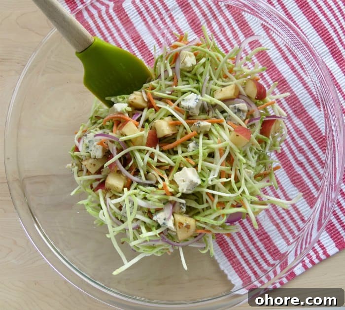 Quick Broccoli Slaw Recipe You Can Make Tonight 4 Broccoli slaw ingredients in a glass bowl with a spatula next to a red napkin