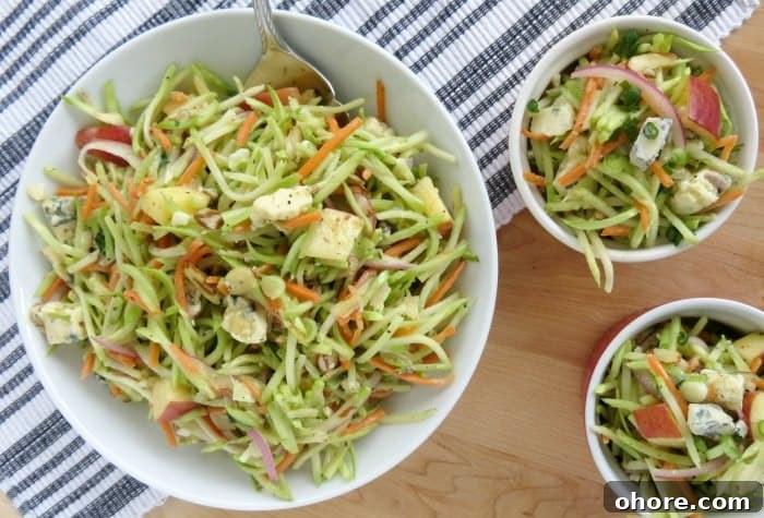 Quick Broccoli Slaw Recipe You Can Make Tonight 7 broccoli slaw in a white serving bowl with a silver spoon next to two smaller bowls on a striped napkin