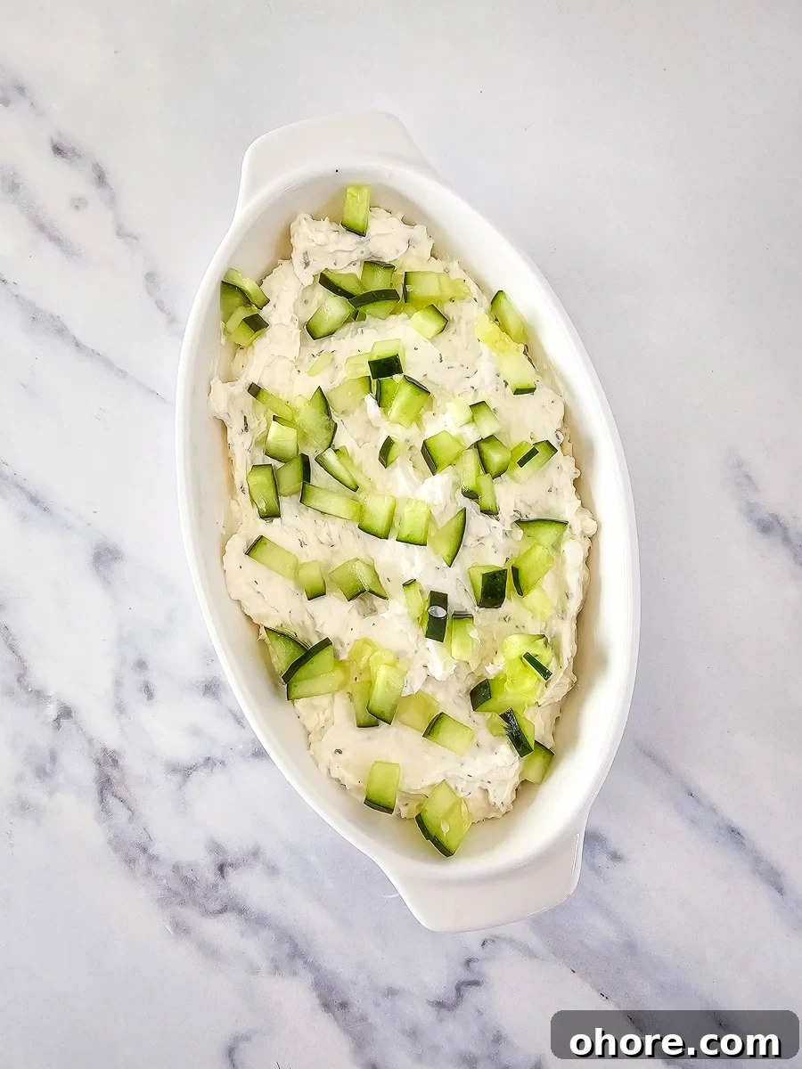 Creamy Vegetable Pizza Dip Recipe for Parties and Game Day 8 Cucumber is spread on top of dip in bowl.