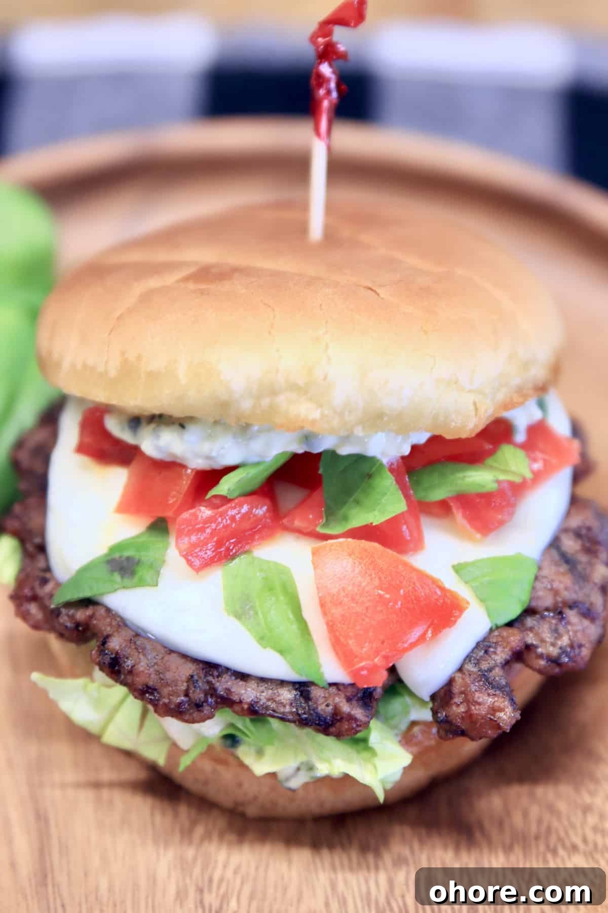 Grilled Caprese Burgers Grilled burger with mozzarella, tomatoes, basil on a wood plate.